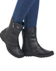 Legs in jeans wearing black leather mid-calf boot with beige accent stitching.