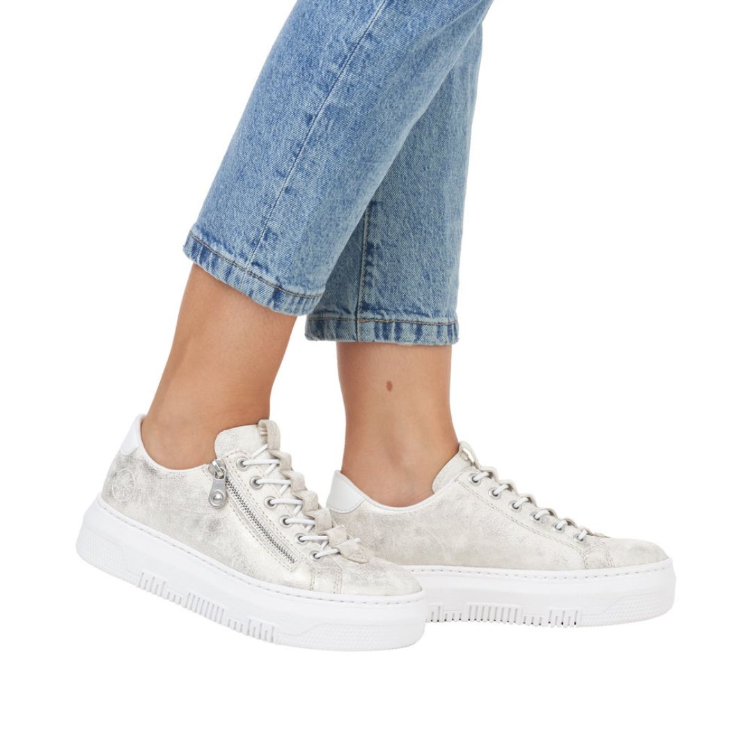 Person in blue jeans and Riekers M1953 gold platform sneakers.
