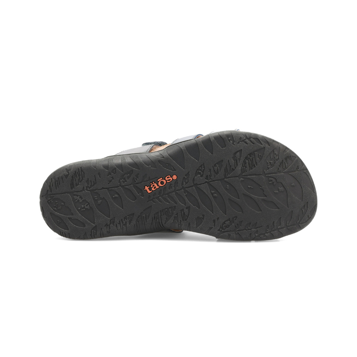 Black leaf pattern outsole of slide sandal with orange Taos logo stamped in middle.