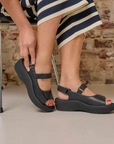 Person wearing black platform sandals with a brick wall background