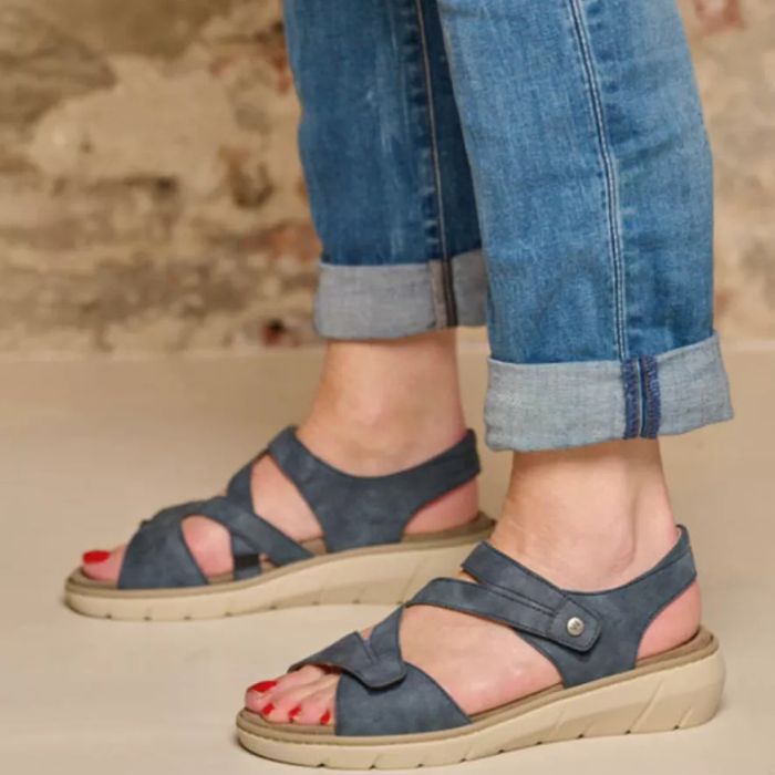Person wearing blue sandals and jeans with a neutral outdoor background