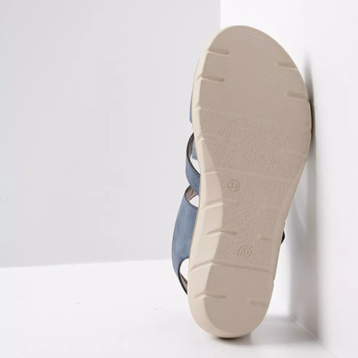 Beige outsole of blue sandal leaning on white wall showing light tread pattern
