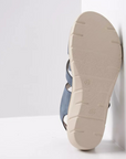 Beige outsole of blue sandal leaning on white wall showing light tread pattern