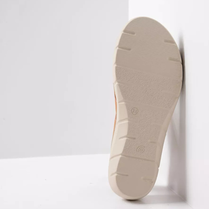 Beige outsole with light tread on backstrap sandal leaning against white wall.