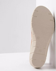 Beige outsole with light tread on backstrap sandal leaning against white wall.
