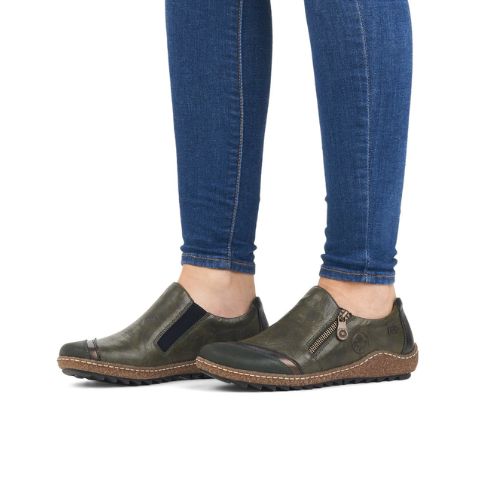 Woman wearing blue jeans and green slip on shoes.