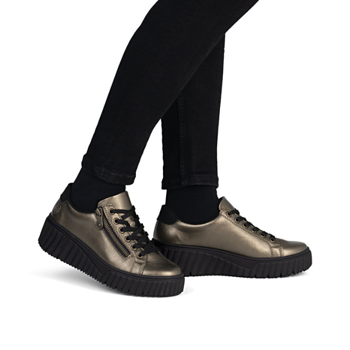 Bronze sneakers with black platform outsoles worn with black pants.