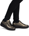 Bronze sneakers with black platform outsoles worn with black pants.