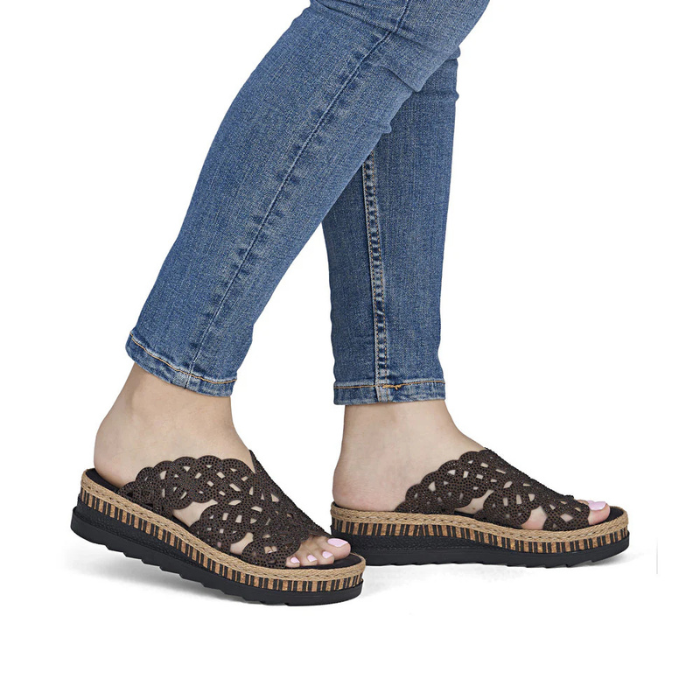 Brown wedge sandals with black rhinestone accents worn with blue jeans.