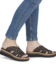 Brown wedge sandals with black rhinestone accents worn with blue jeans.