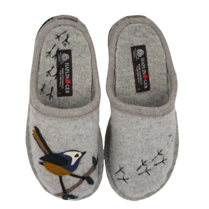 A pair of light gray felt slip-on slippers with embroidered bird with blue, yellow, and white details on a branch with bird footprints over the footbed on one slipper, while the other has small black stitched bird footprints.