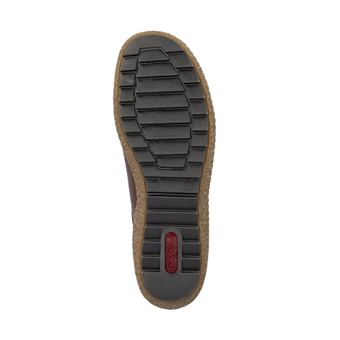 Top-down view of a shoe sole showing a black treaded outsole with a tan cork-like midlayer and a small red Rieker logo near the heel, on a white background.