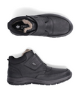Pair of black leather Velcro shoes with fur cuff, black Rieker logo'd footbed and black treaded outsole.