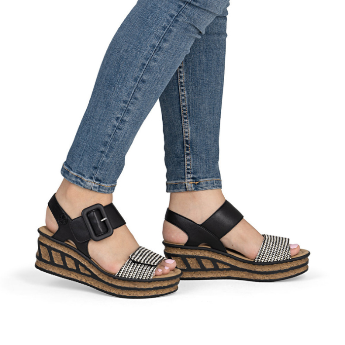 Black wedge sandals with faux cork outsoles worn with blue jeans.