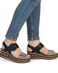 Black wedge sandals with faux cork outsoles worn with blue jeans.