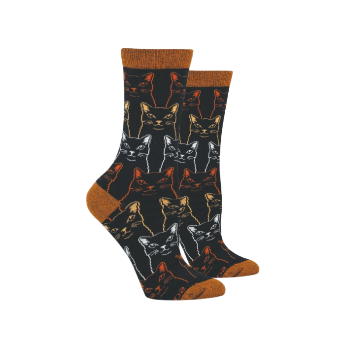 A pair of crew socks with a black background featuring a repeating pattern of sketched style cat faces in orange, white, and grey.