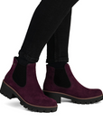Purple suede Chelsea boots worn with black pants.