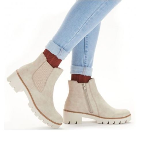 Woman in blue jeans and burn orange socks wearing beige lugged Chelsea boots.
