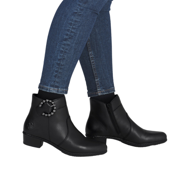 Black ankle boots with decorative beaded buckle worn with blue jeans.