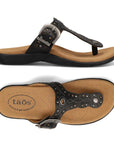 Pair of Black T-strap sandal with embroidery, rivets and grommet detailing and an antiqued adjustable buckle with Taos logo'd beige footbed and black outsole.