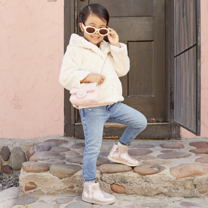 Child wearing a light pink puffer jacket, jeans, and glittery pink leopard print ankle boots standing on stone steps.