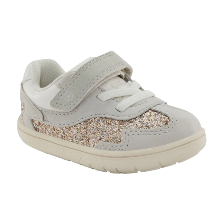 A toddler's light gray sneaker with a glittery gold and silver side panel, white elastic lacing, and a hook-and-loop strap closure.