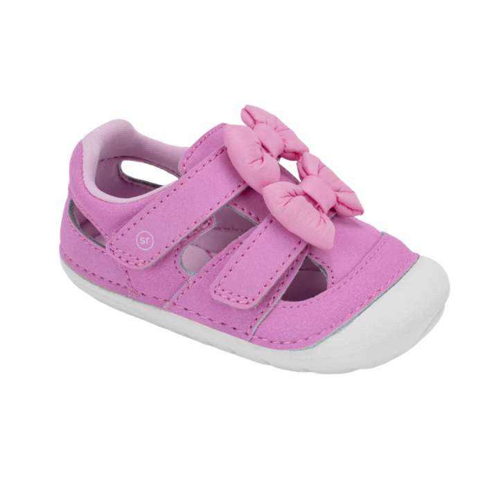 A pink toddler sandal with two hook-and-loop straps, a large matching bow on the toe and white soft bottom outsole.