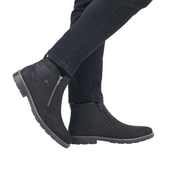 Legs in black jeans wearing black ankle boot with silver side zipper closure.