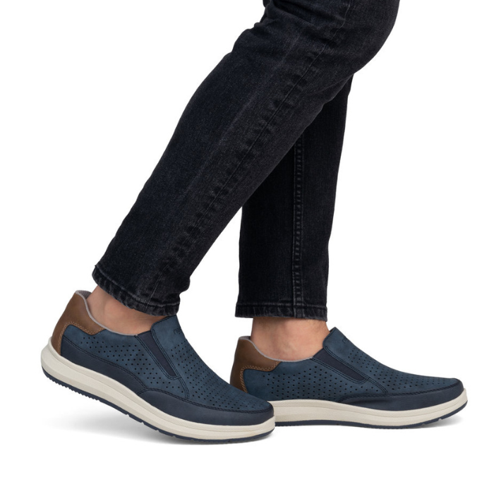 Navy slip-on shoes with brown accents worn with black jeans.