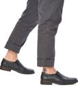 Legs in grey cuffed pants wearing black leather slip on shoe with toe cap.