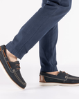 Navy blue boat shoes with brown accents worn with navy pants.