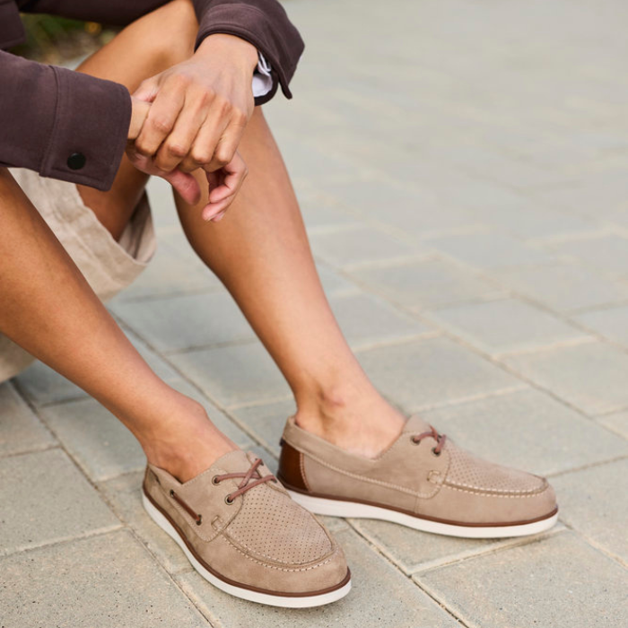 Person wearing brown boat shoes sitting on a stone pathway.
