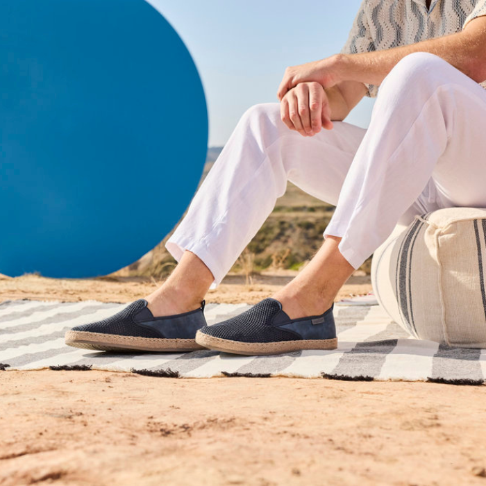 Person wearing navy loafers sitting on a striped blanket with a blue circle sculpture in the background.