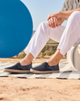 Person wearing navy loafers sitting on a striped blanket with a blue circle sculpture in the background.