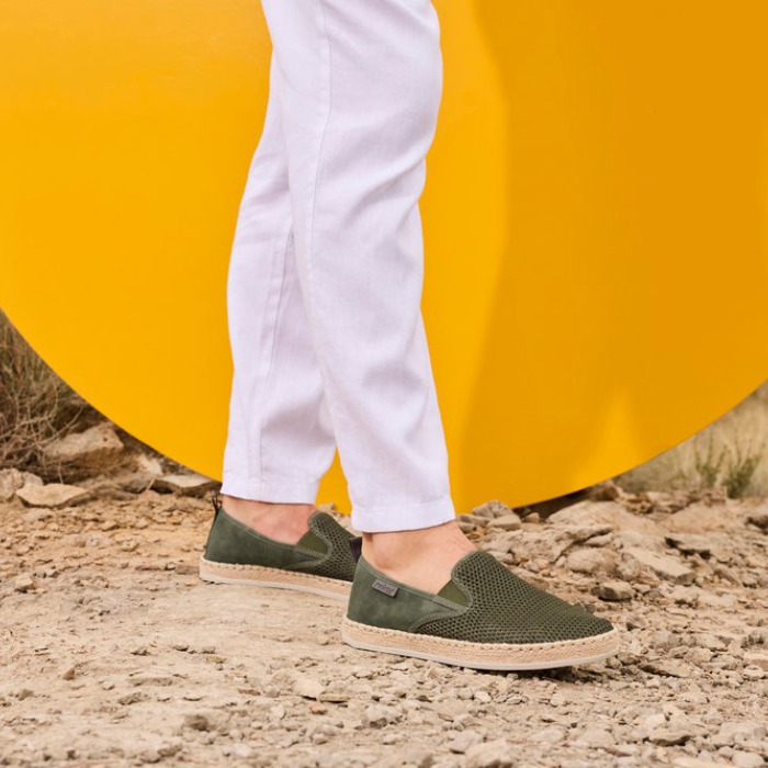 Person wearing green loafers with a yellow background and dirt path.