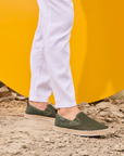 Person wearing green loafers with a yellow background and dirt path.