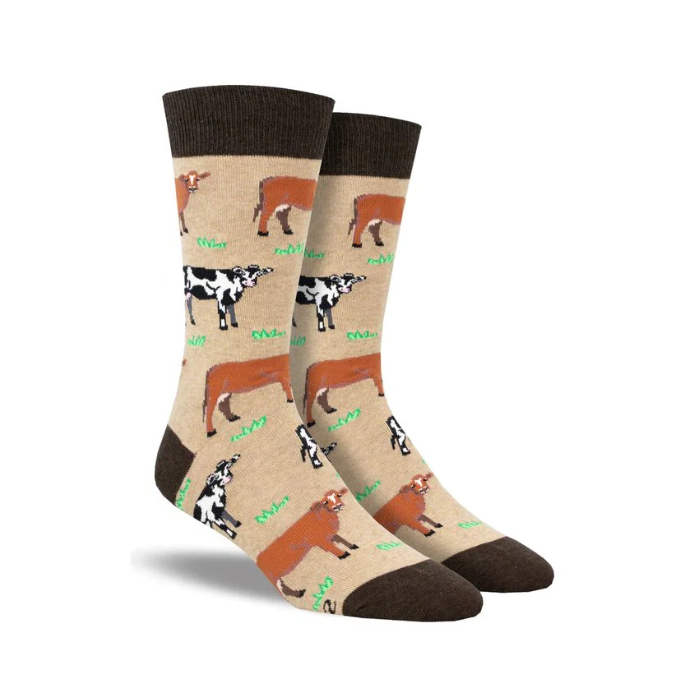 Socksmith Men's Mooove Over Socks featuring a beige background with playful cow patterns in black, white, and brown. Crew-length design with dark brown accents at the toe, heel, and cuff.