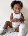 Baby girl playing on mattress with grey leather bunny shoes on.