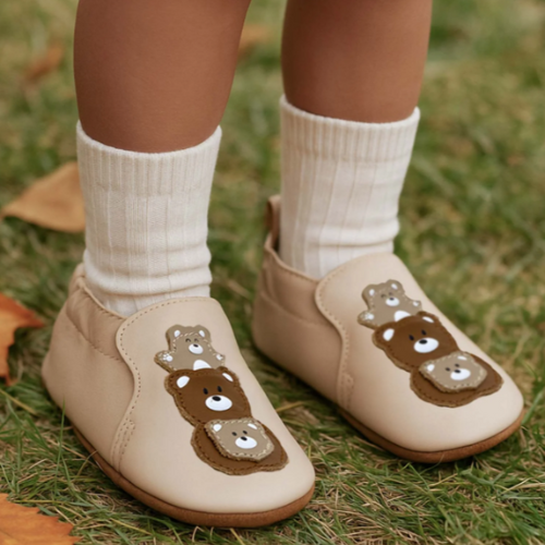 Toddler wearing Soft Sole leather shoes with bear designs and with white socks on a grassy background