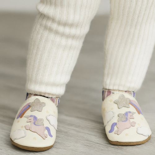 Child wearing white soft pants and leather soft shoes with unicorn and star designs.