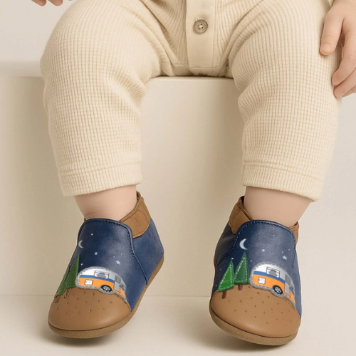 Blue and brown baby's shoes with camper design worn by a child sitting on a beige ledge.