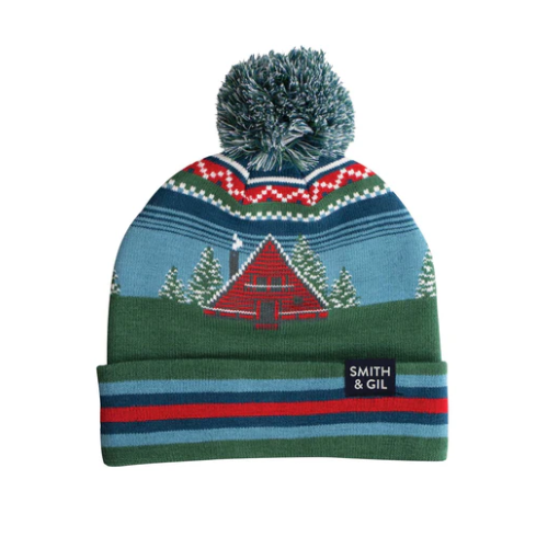 Knitted beanie with a design of a cabin and trees, a pom-pom on top and Brand 'Smith & Gil' tag on cuff.