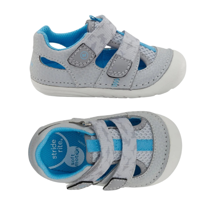 Pair of light grey toddler sandals with two hook-and-loop straps, blue accents, blue Stride Rite logo'd footbed and white outsole.