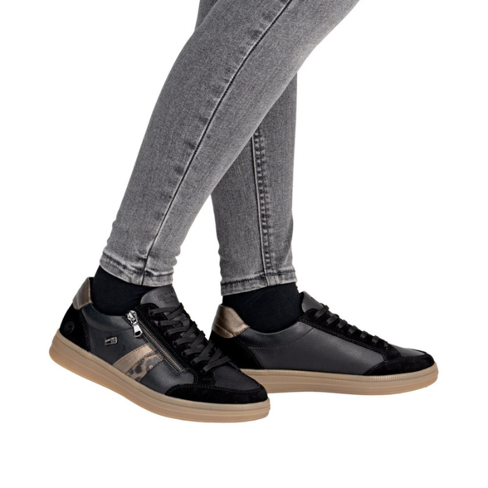 Black sneakers with bronze and cheetah accents and tan soles worn with gray jeans. 
