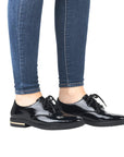 Legs in denim wearing black patent lace derby with gold insert in heel.