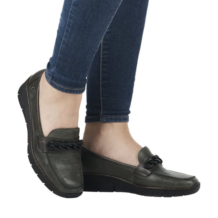 Legs in jeans wearing green leather wedge shoe with chain detailing on top.
