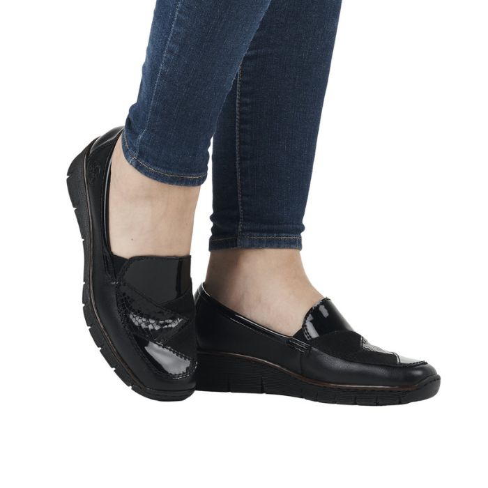 Legs in jeans wearing black wedge loafer with black patent and croco detailing on vamp.