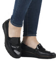 Legs in jeans wearing black wedge loafer with black patent and croco detailing on vamp.