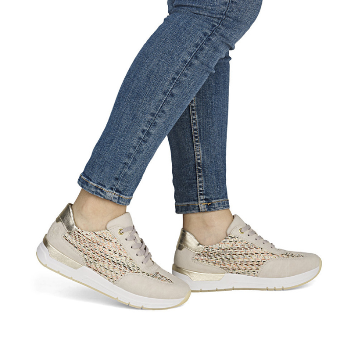 Beige sneakers with woven side panels worn with blue jeans.