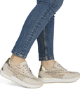 Beige sneakers with woven side panels worn with blue jeans.
